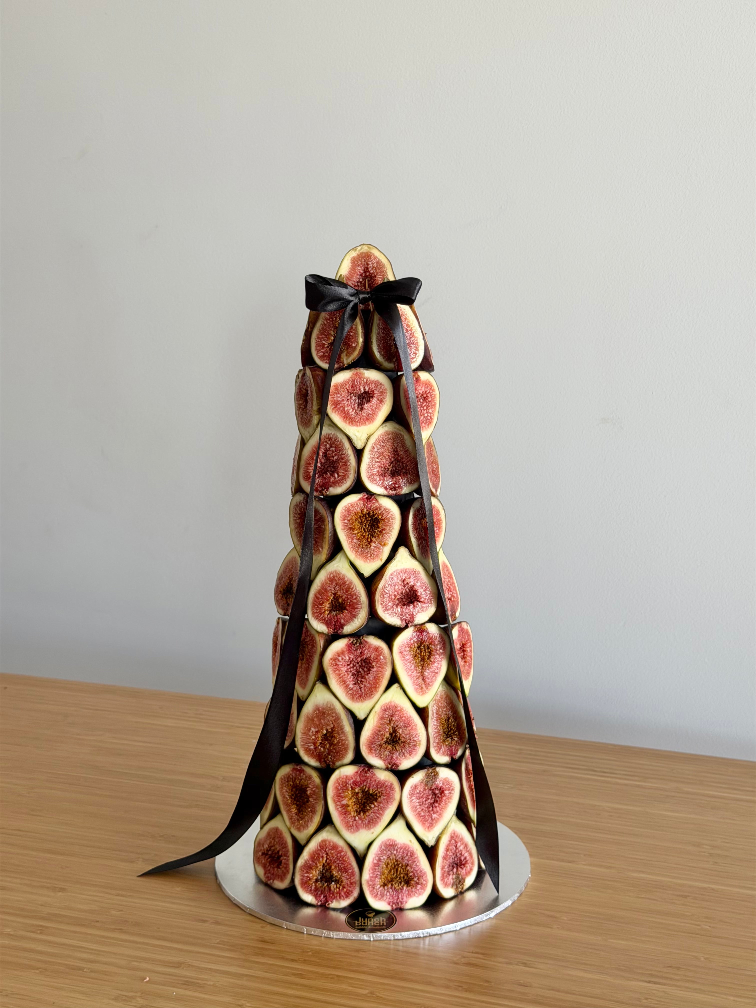 Handcrafted fig tower made from fresh seasonal figs arranged on a cone stand with black ribbon, luxury event centrepiece.